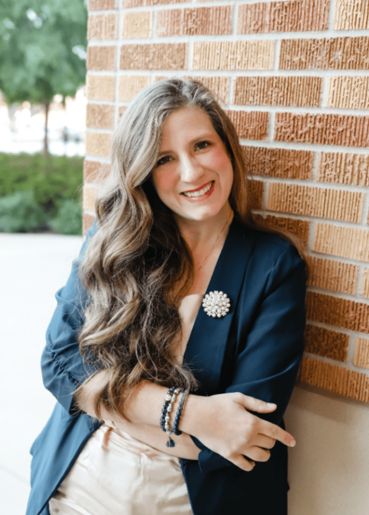 Rachel, founder of RJ Marketing Solutions, smiling confidently while leaning against a brick wall, representing approachable and professional marketing leadership.